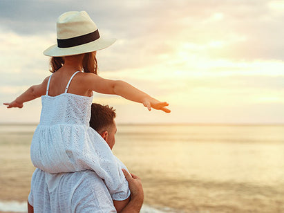 girl on her dads shoulders at the beach