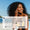 A smiling woman on the beach applies Edelweiss Sun Cream with Tan Accelerator SPF15 to her cheek next to a customer review.