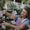 A smiling mature woman gardens outdoors near pink flowers, highlighting benefits of Age Defy+ Collagen Boost Vitamin C Serum.