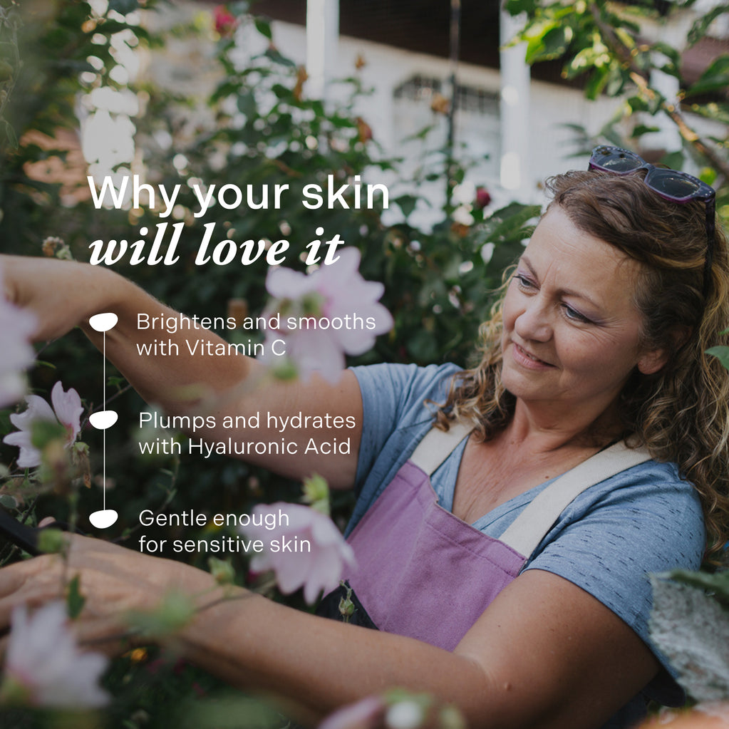 A smiling mature woman gardens outdoors near pink flowers, highlighting benefits of Age Defy+ Collagen Boost Vitamin C Serum.