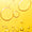 Close-up of golden oil droplets and larger bubbles suspended in a bright yellow liquid.